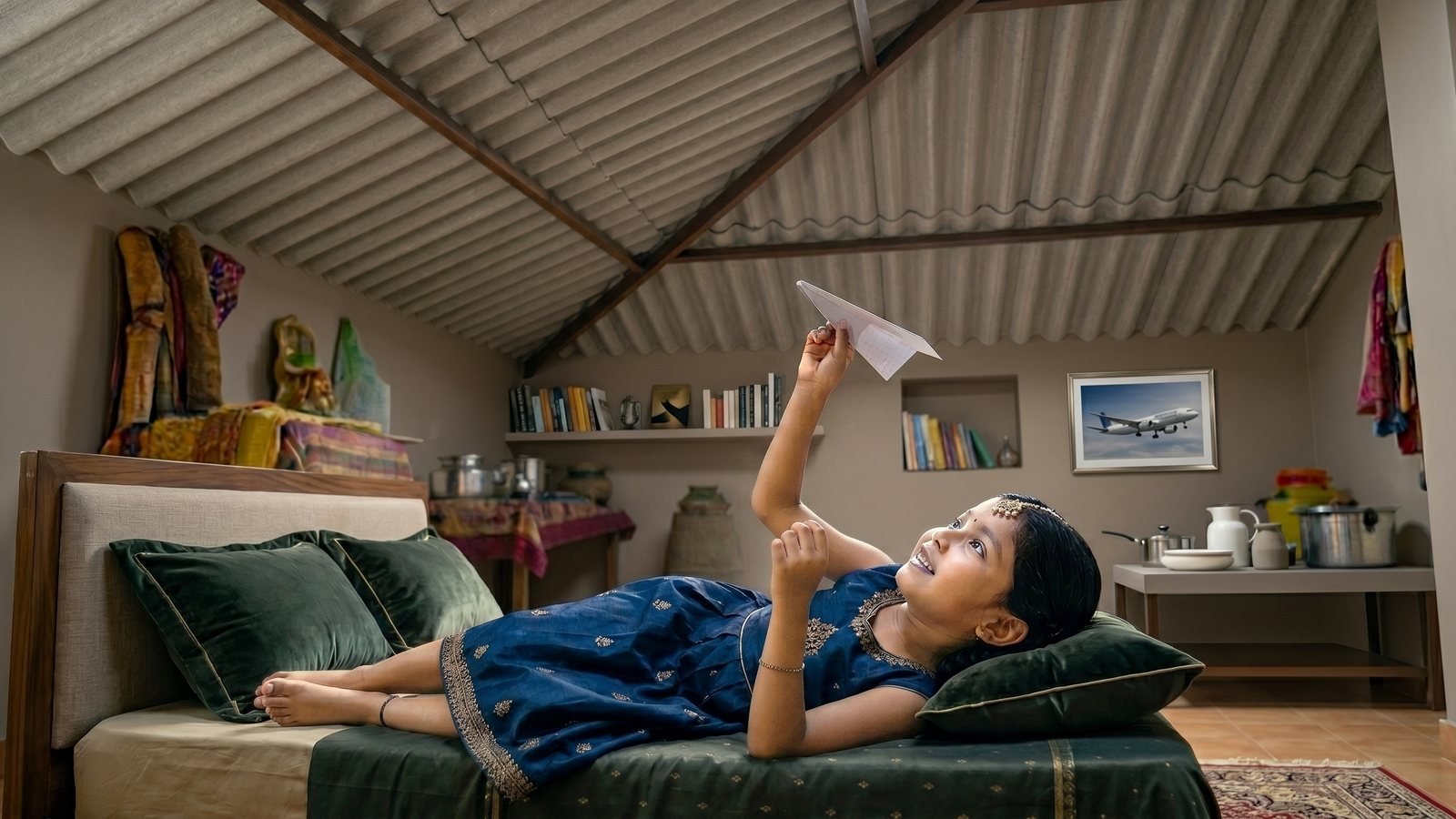AI video marketing case study: a girl lies on a bed under a CHARMINAR roof, holding up a paper plane, in a key frame from 'Ye Chhat' for BirlaNu