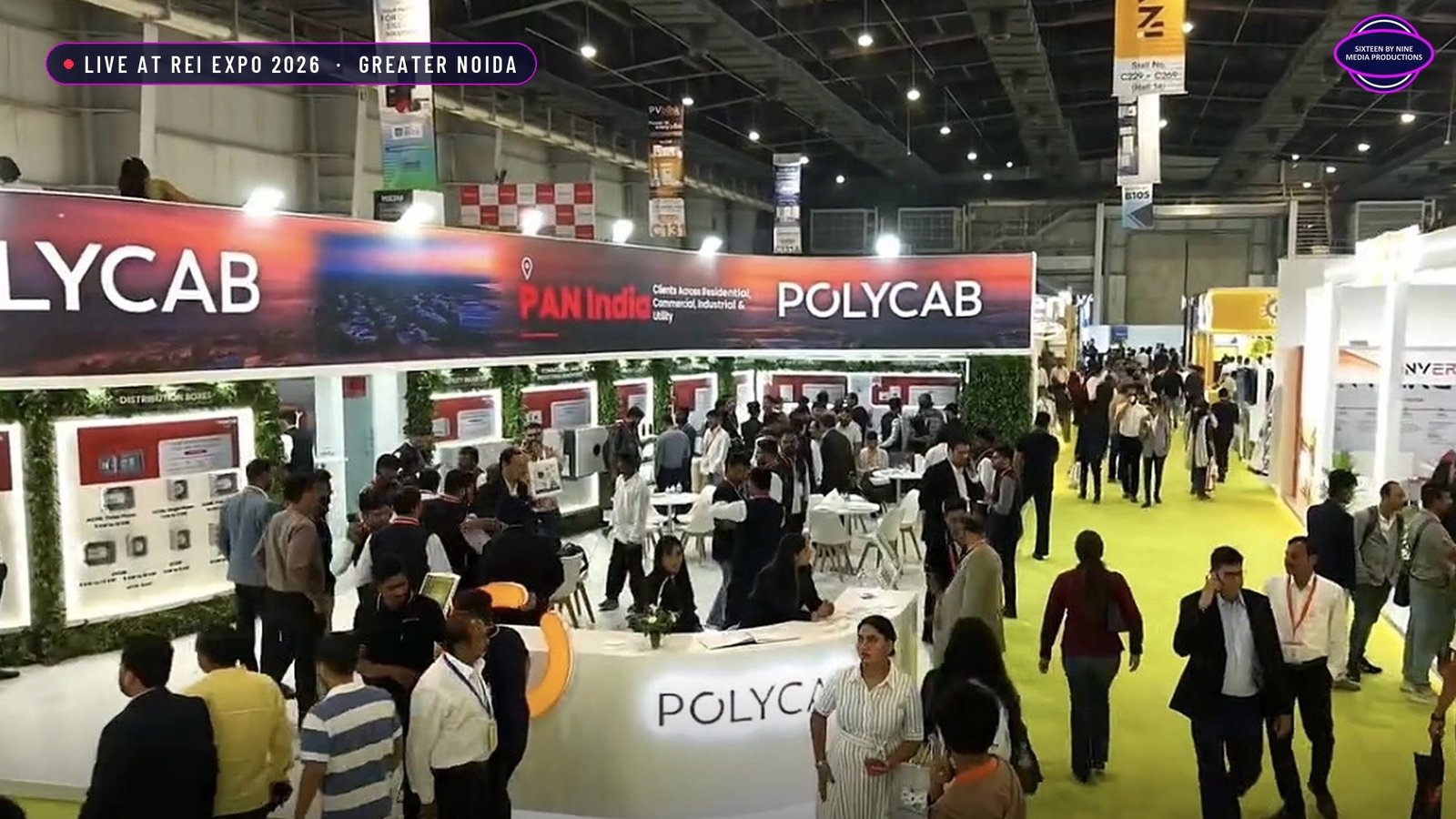 Polycab Solar stall at REI Expo 2026, crowded aisle, with its 23 m LED strip running above